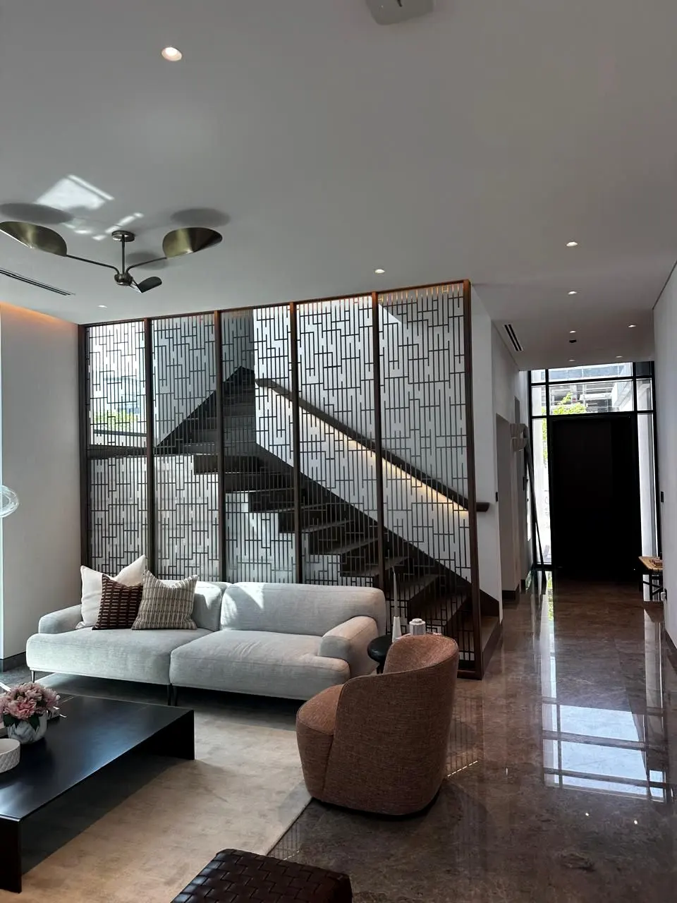 Double-height living room at Alaya with a bronze decorative metal screen enclosing a floating timber staircase