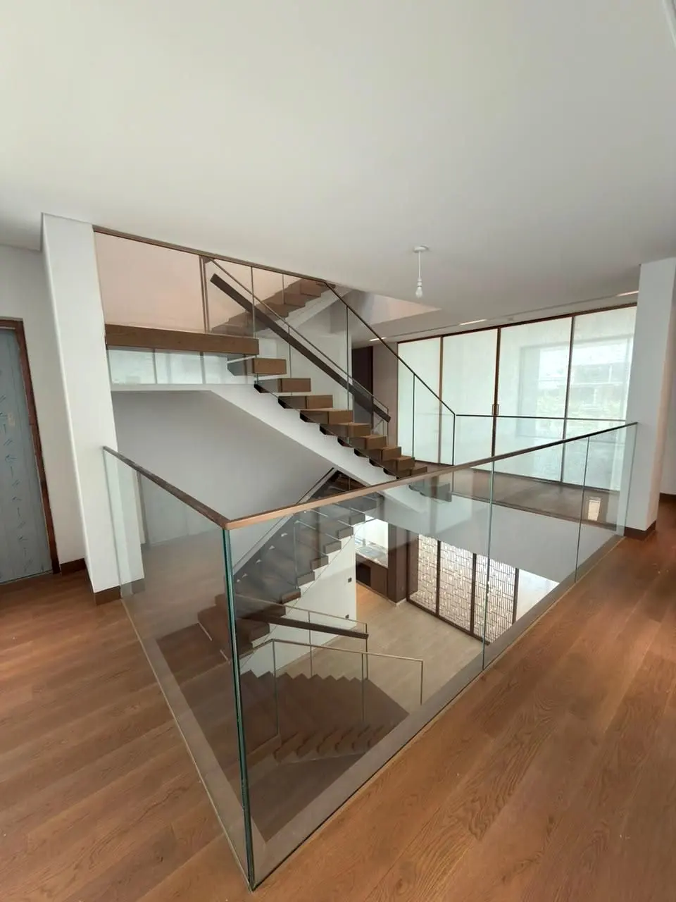 Open-riser timber staircase with a frameless glass balustrade rising through a bright villa hall