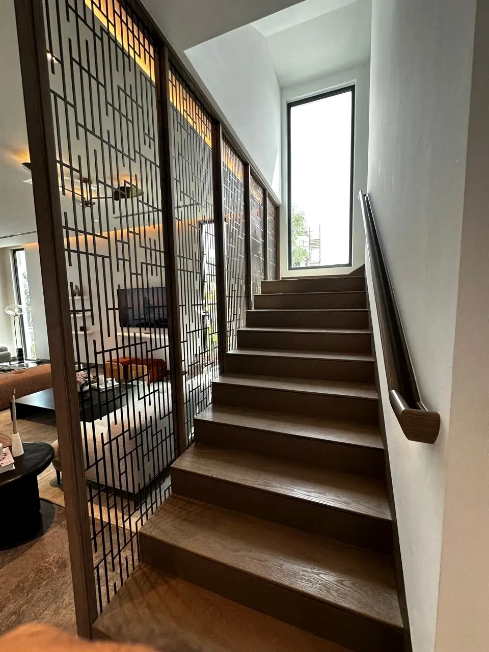 Timber stair flight beside a full-height bronze screen with a wall-mounted handrail