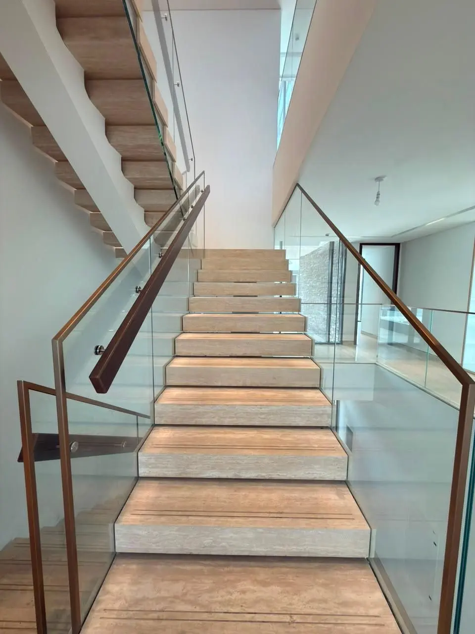 Straight flight of cantilevered stone treads between frameless glass balustrades with a bronze handrail