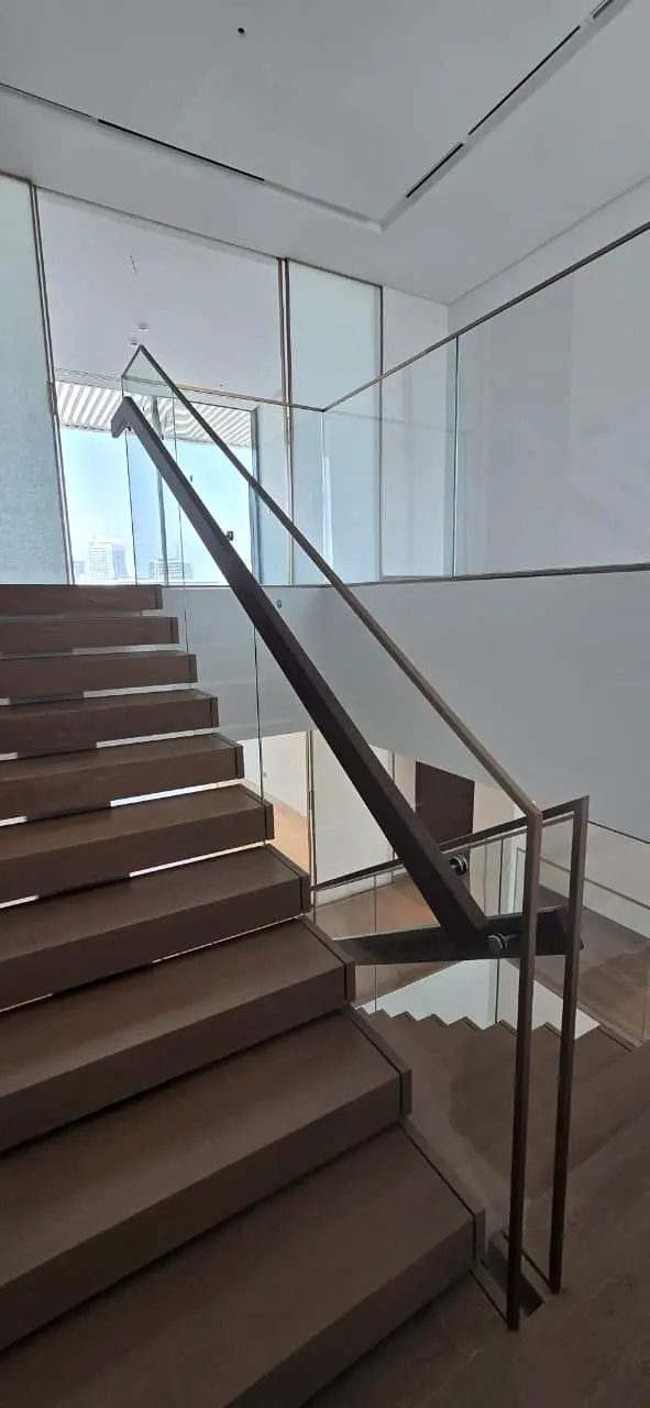 Timber stair with glass balustrade and dark handrail seen from the upper landing