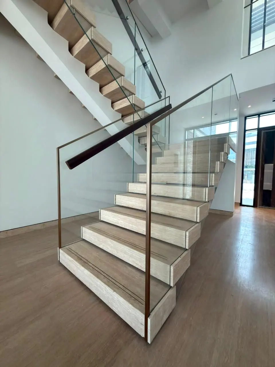 Stone-clad floating stair with glass balustrade and bronze top rail