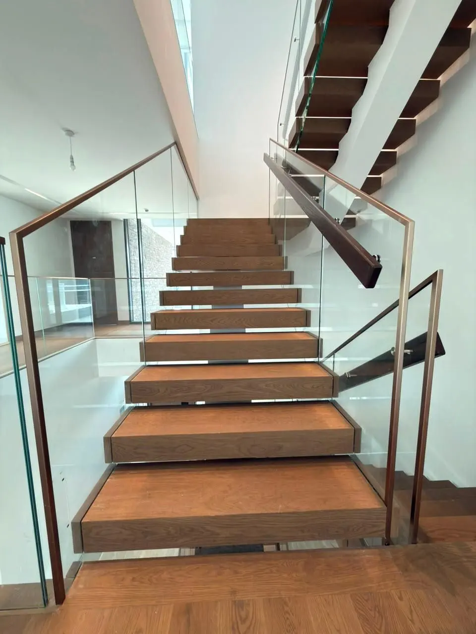 Timber treads climbing between glass balustrades with a slim bronze handrail