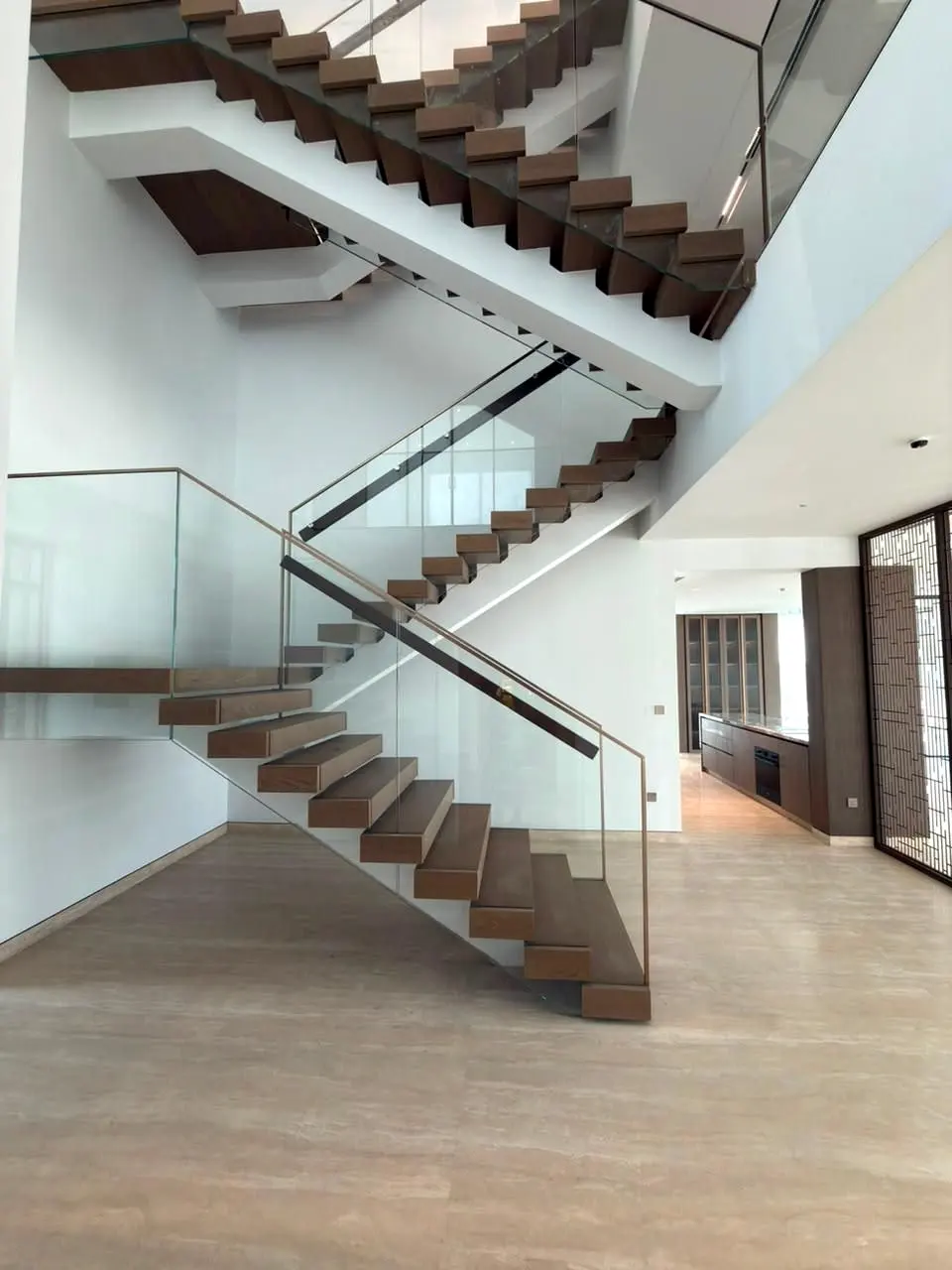 Switchback timber stair with glass balustrade over a stone-floored hall