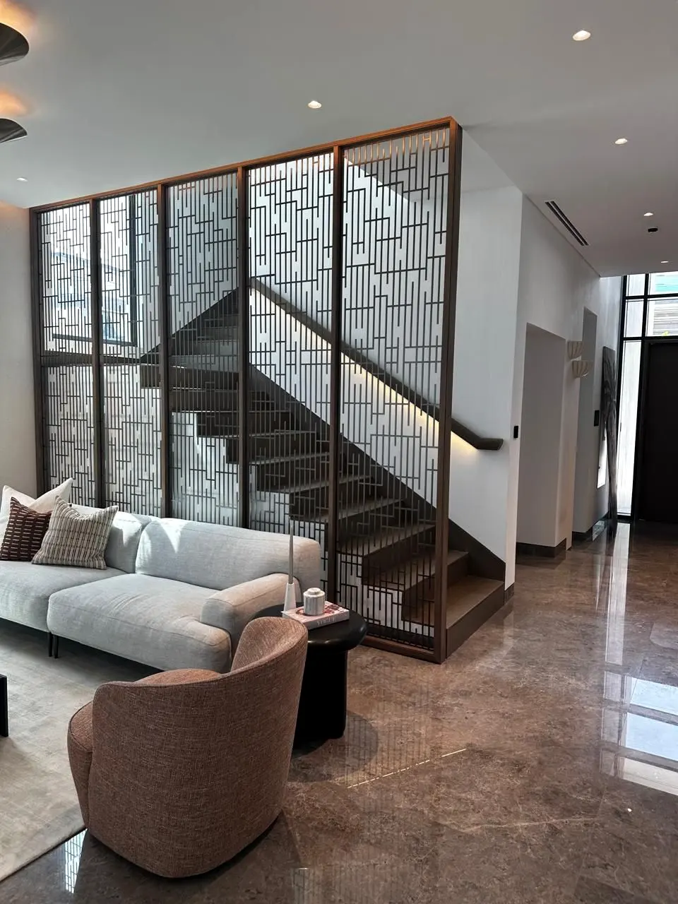 Bronze metal screen and floating timber stair behind a furnished lounge at Alaya, Tilal Al Ghaf