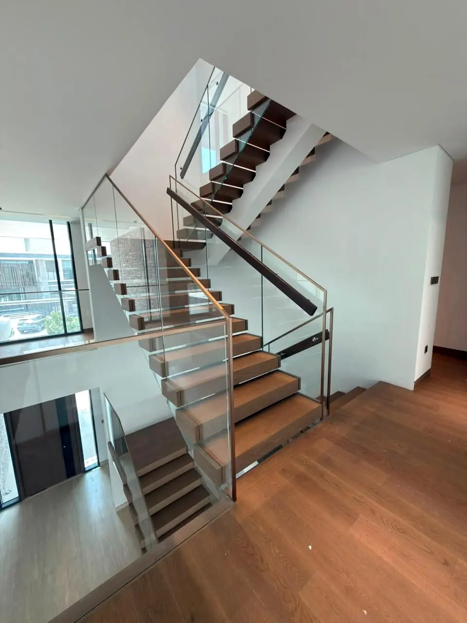 Timber stair rising past glass balustrades toward the upper floor