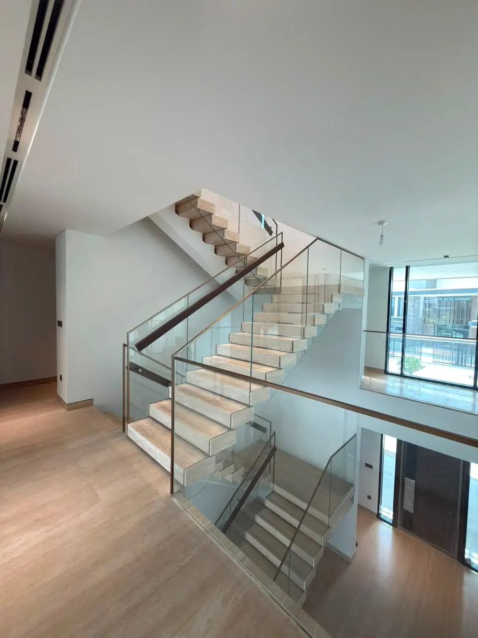 Timber stair and glass balustrade over a stone-floored hall