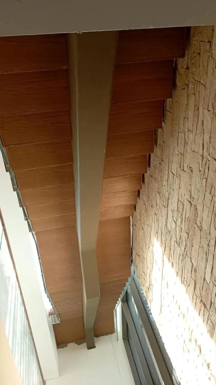 Underside of a timber-clad staircase beside a stone wall